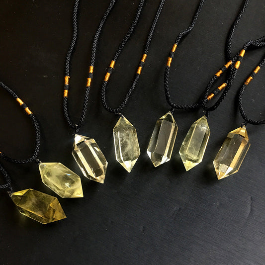 Golden citrine polished pointed pendants on black cords against a dark background