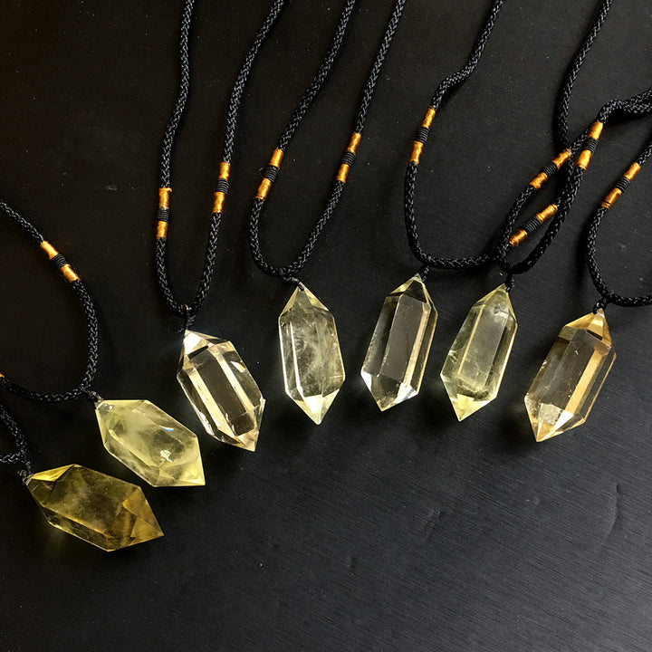 Golden citrine polished pointed pendants on black cords against a dark background
