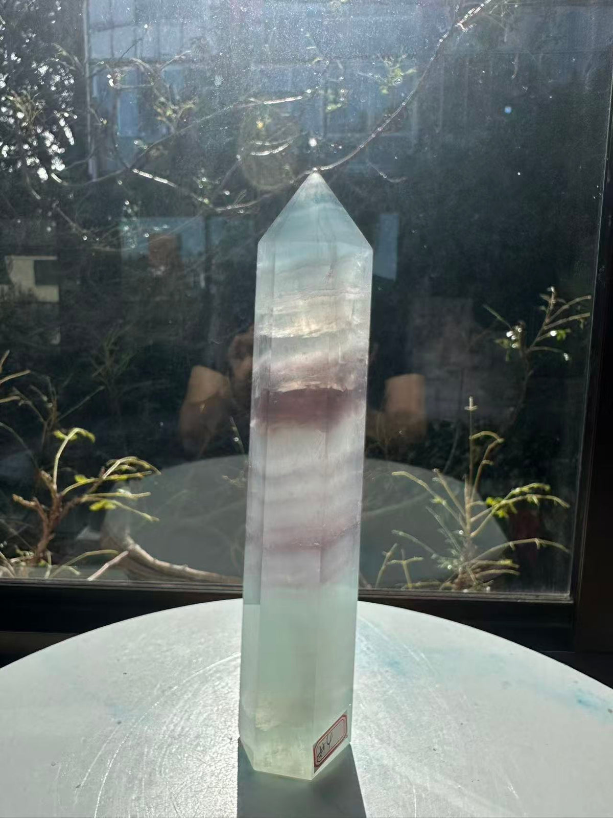 Translucent 23cm tall green fluorite point with prominent horizontal growth layers and a light-reflecting finish, weighing 0.973kg.