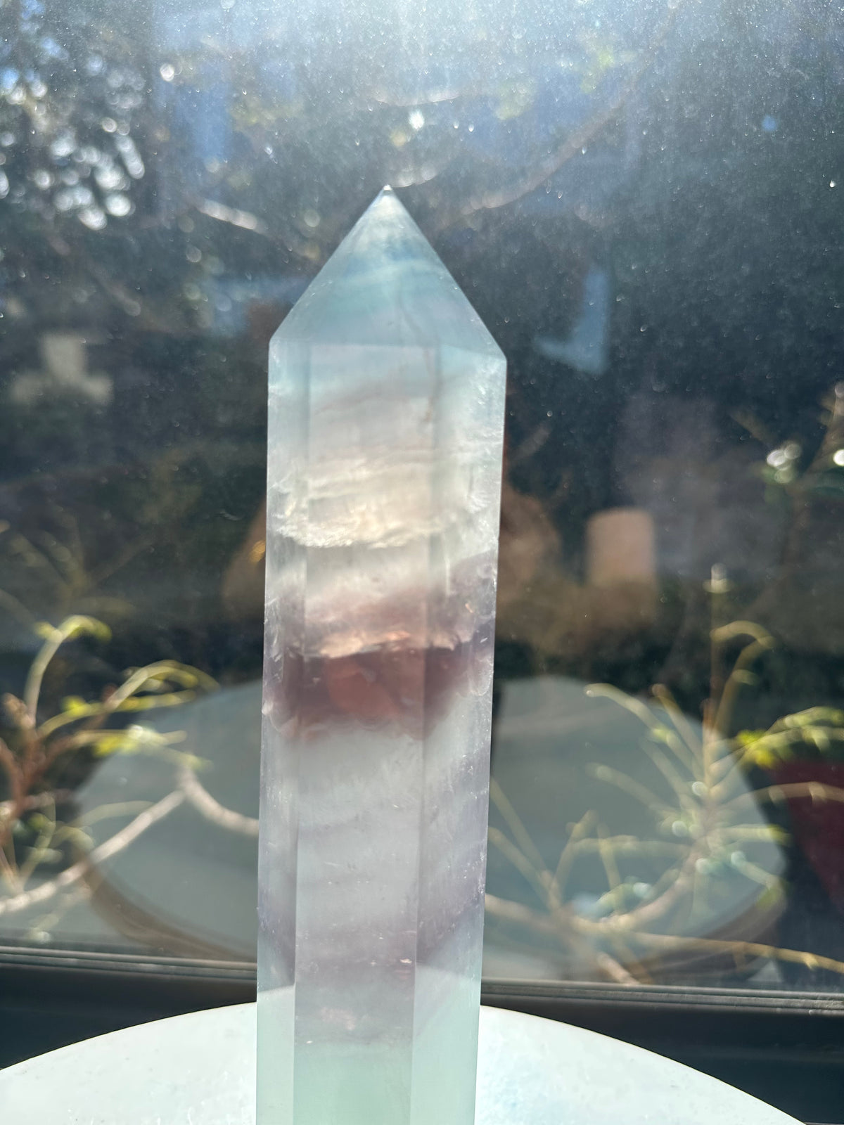 Translucent 23cm tall green fluorite point with prominent horizontal growth layers and a light-reflecting finish, weighing 0.973kg.