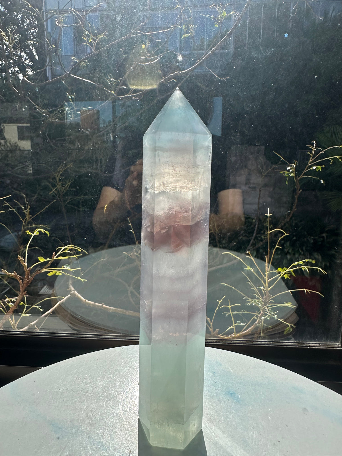 Translucent 23cm tall green fluorite point with prominent horizontal growth layers and a light-reflecting finish, weighing 0.973kg.