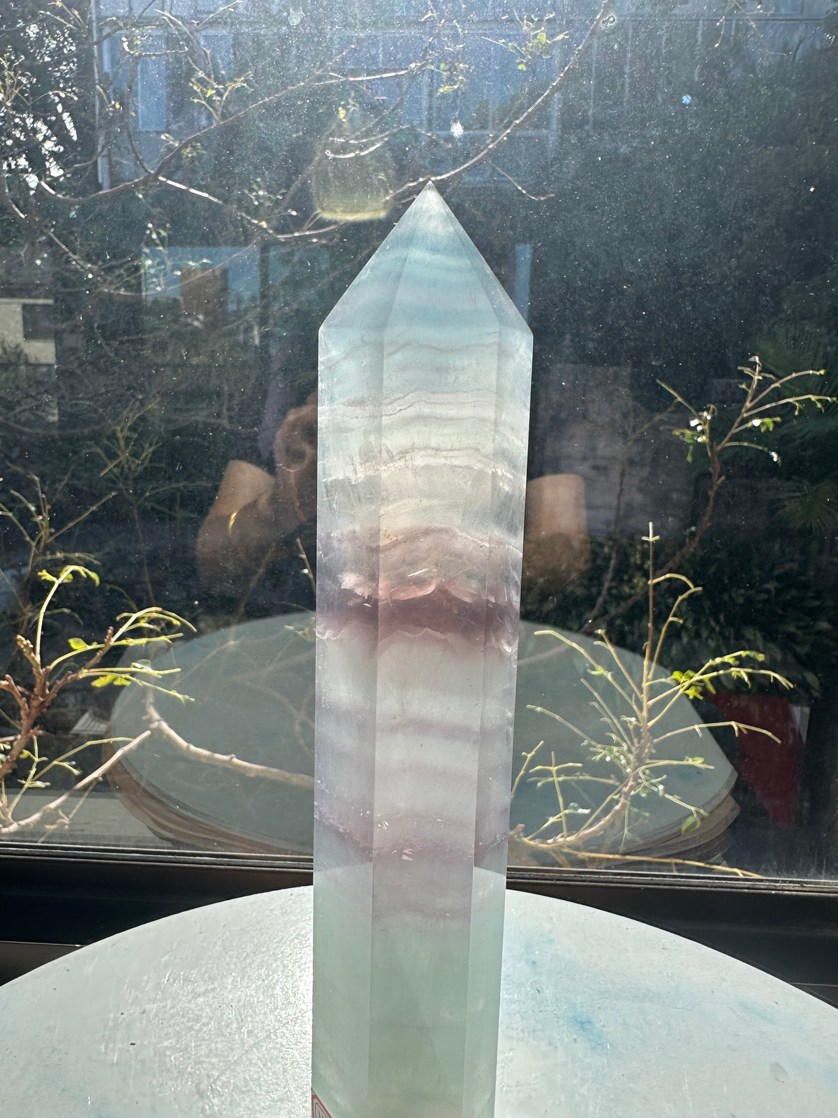 Translucent 23cm tall green fluorite point with prominent horizontal growth layers and a light-reflecting finish, weighing 0.973kg.
