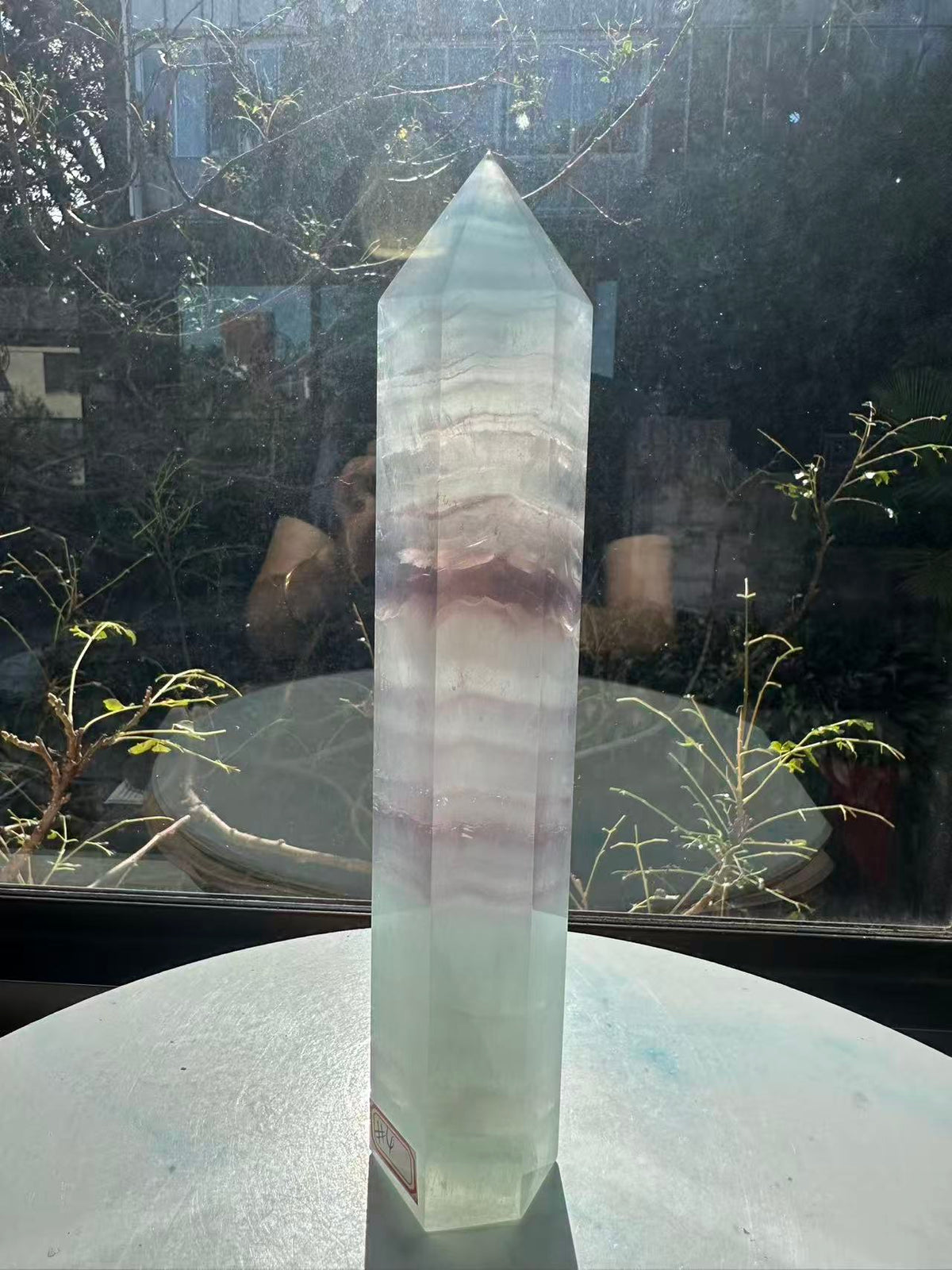 Translucent 23cm tall green fluorite point with prominent horizontal growth layers and a light-reflecting finish, weighing 0.973kg.