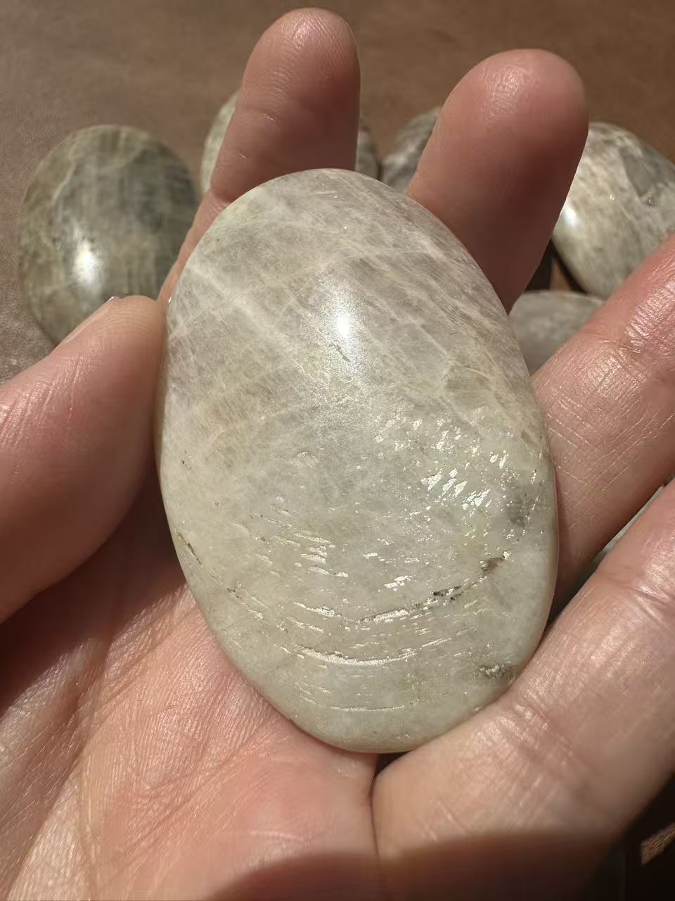 Natural Rainbow Moonstone palm stone with polished finish and angle-dependent flash