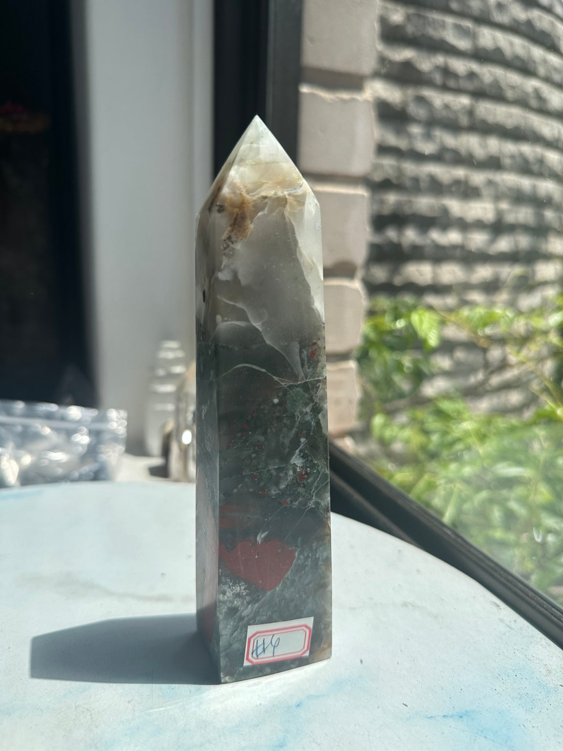 Unedited original front photograph of exact No.4 African bloodstone tower, 433g, with pale upper section and curved red patch in window light.