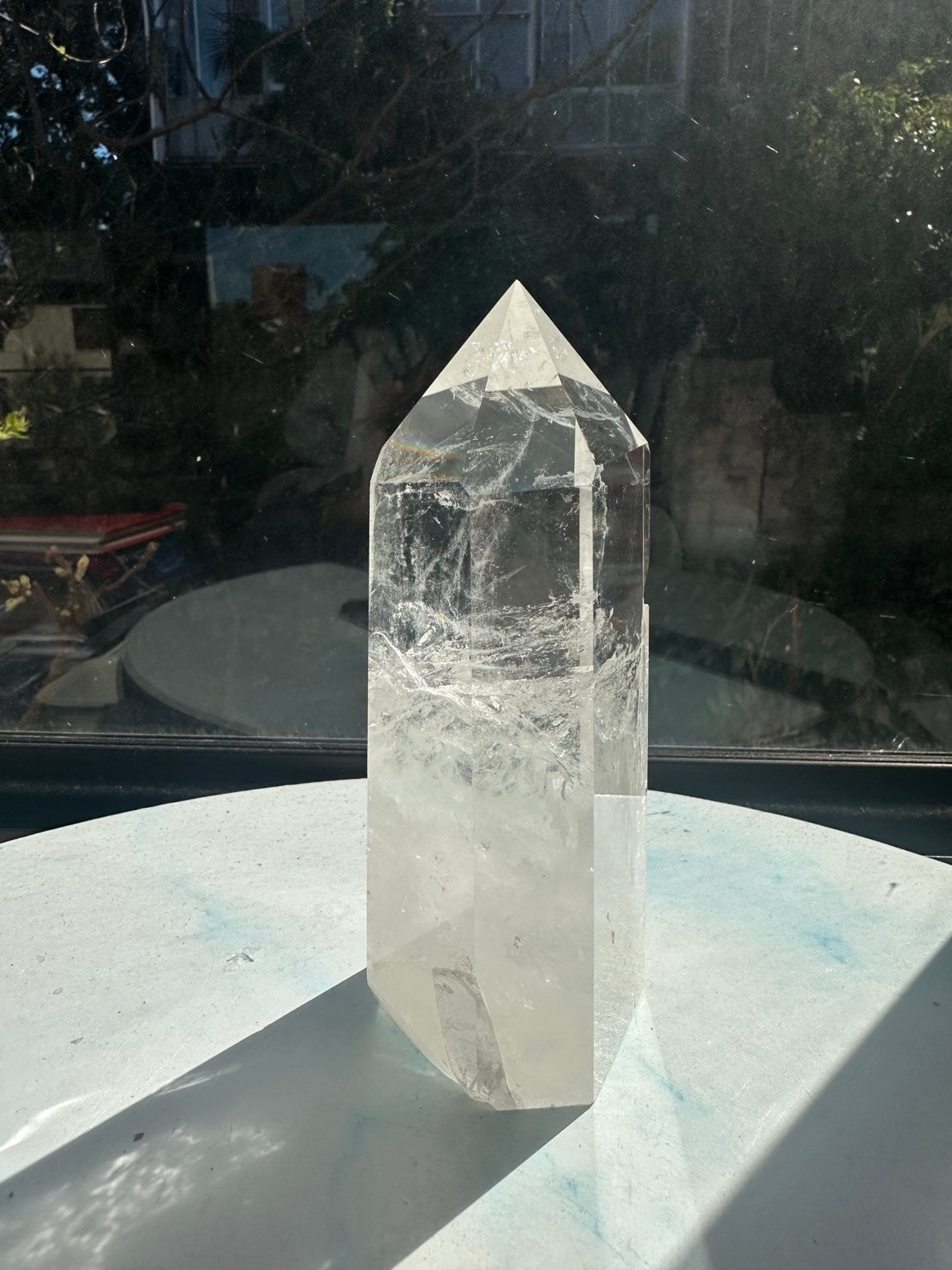 Rotated view of the clear quartz tower showing fine internal fracture lines, polished faces and the cloudy white lower portion beside a window.