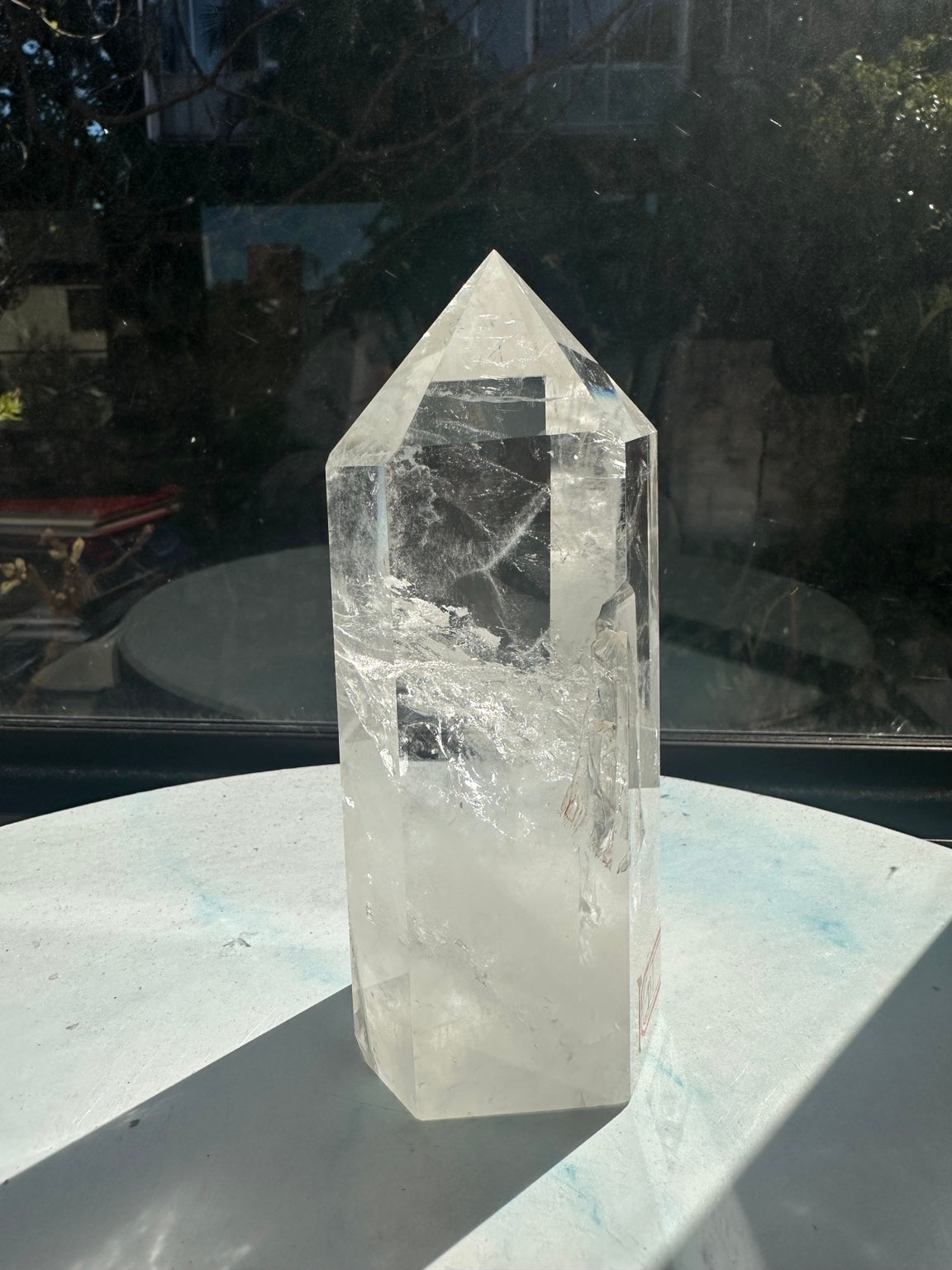 Side of the same Brazilian quartz point showing its polished facets, small darker inclusions and wispy internal textures in natural sunlight.