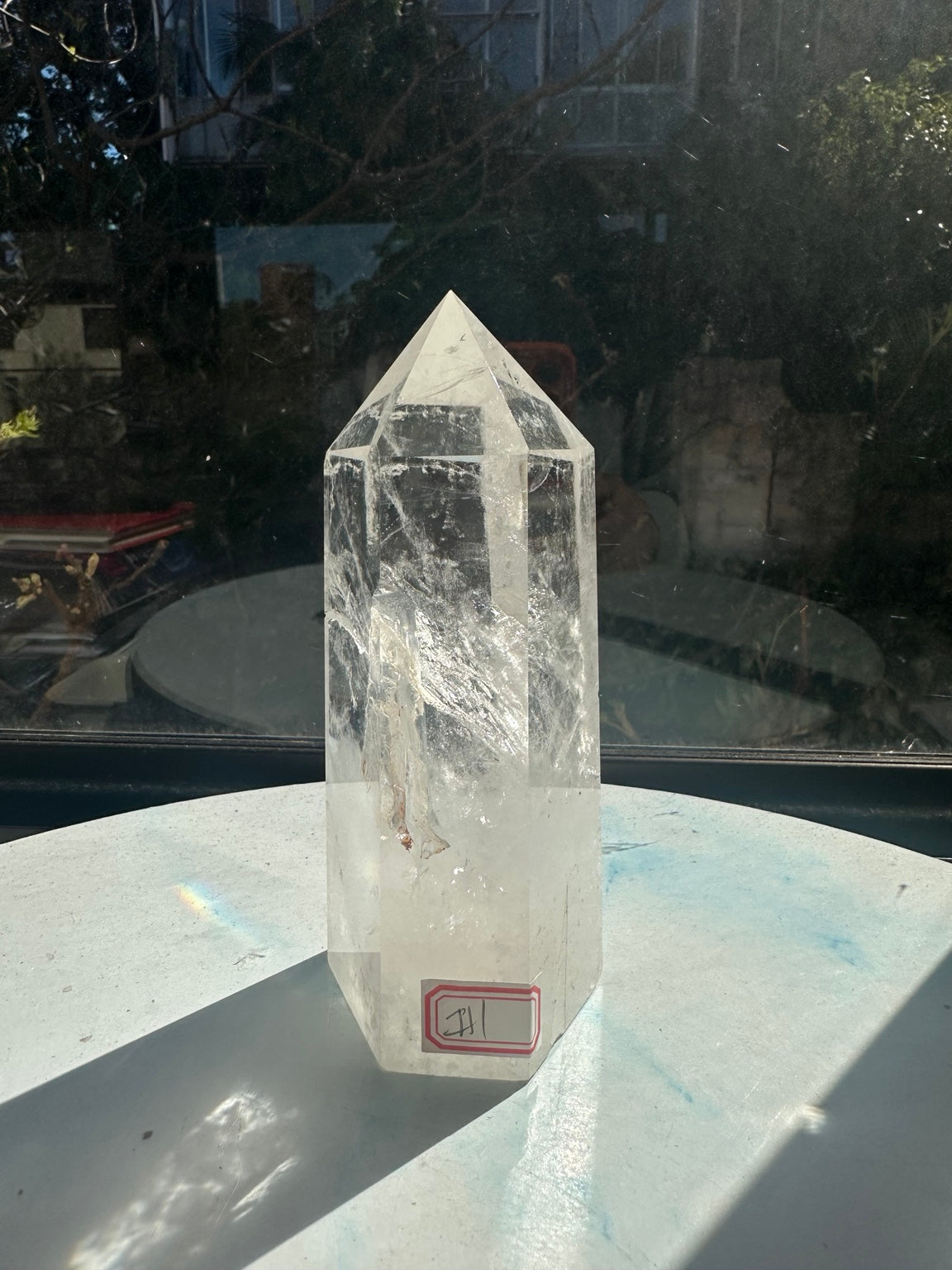 Slightly turned front view of the quartz point, revealing its red sticker, polished edges and cloudy lower section.