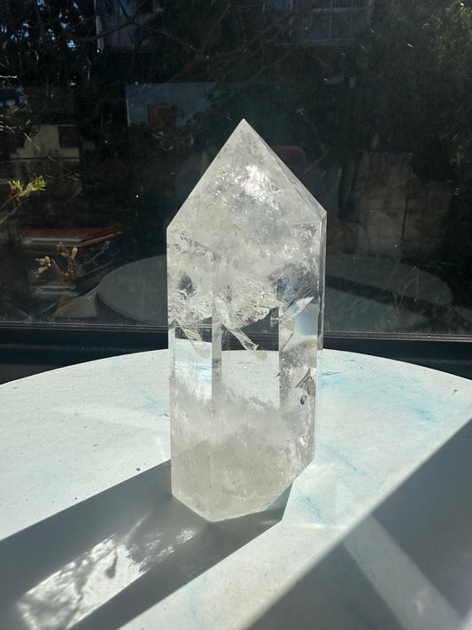 Brazilian clear quartz tower #2 in sunlight, showing its polished point, broad transparent facets, sweeping white internal veils and cloudy base. Exact 624g piece, approximately 13.8cm tall.