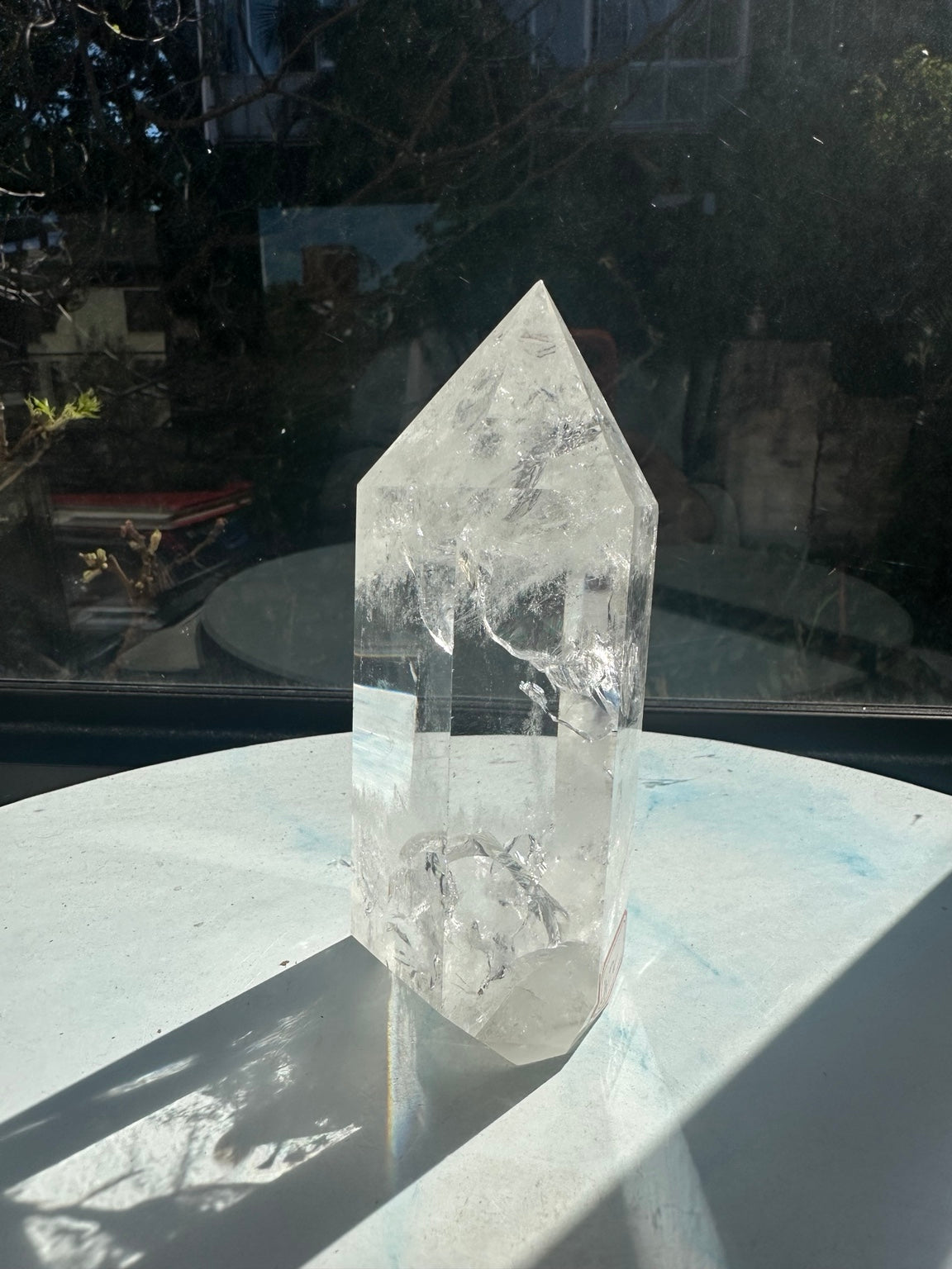 Narrow angled view of the same polished quartz tower, with a broad curved internal veil, clear faces and part of the red label near the base.