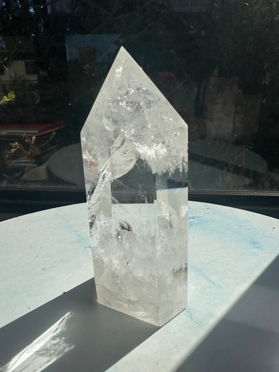 Side angle of the clear quartz tower showing a sweeping internal fracture plane, white veils and small darker inclusions near the lower section.