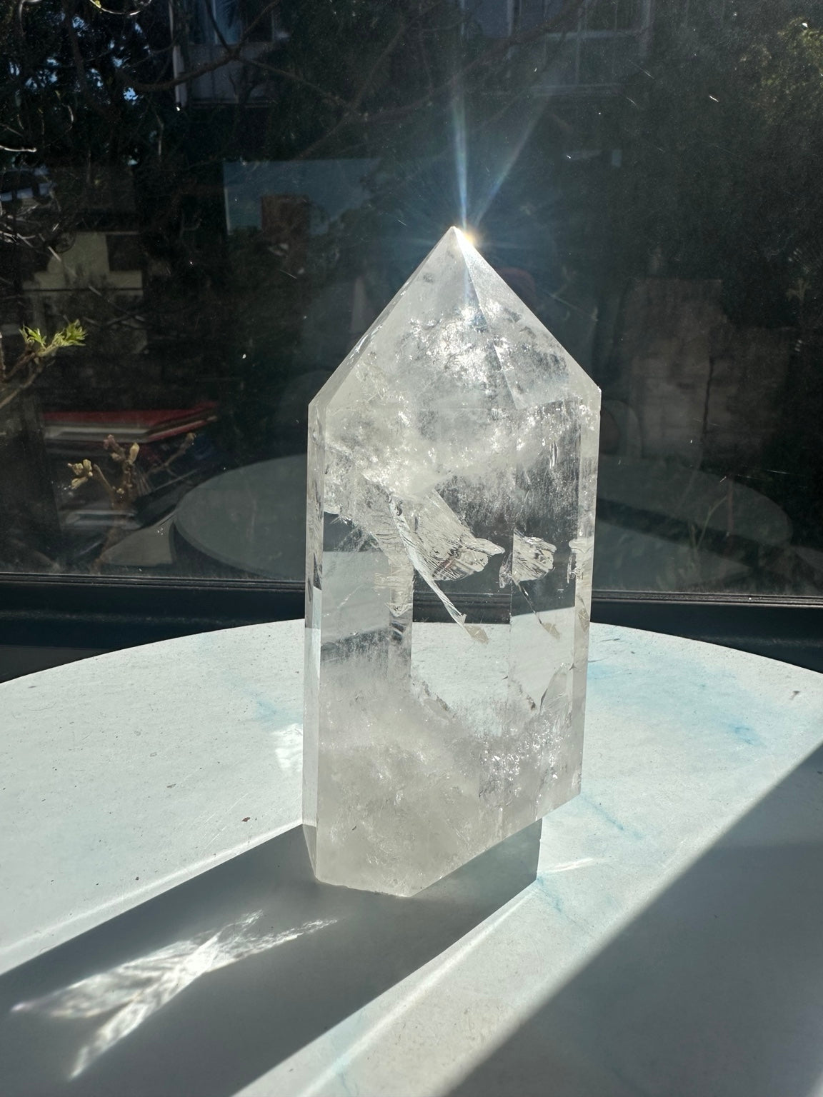 Sunlit angle of the Brazilian clear quartz point showing a bright reflection at its tip, polished facets and white internal fracture textures.