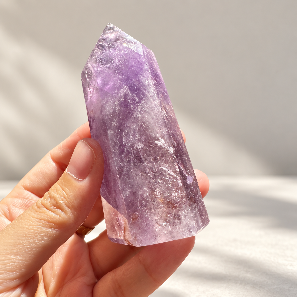 Brazilian Amethyst tower held in a hand to show its proportions, polished point and natural internal veils