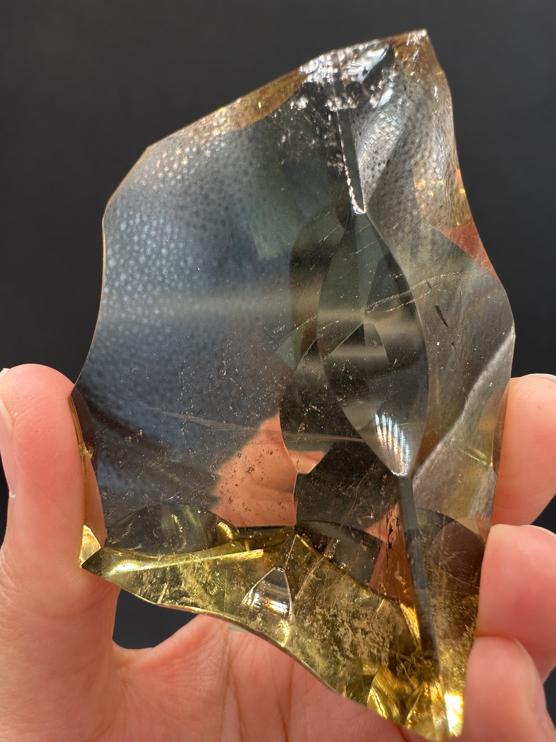 Brazilian citrine freeform No.7, 117g, approx. 7 × 5cm; close view of the curved right edge, natural internal lines and the golden lower section, held in the original hand against a charcoal background.