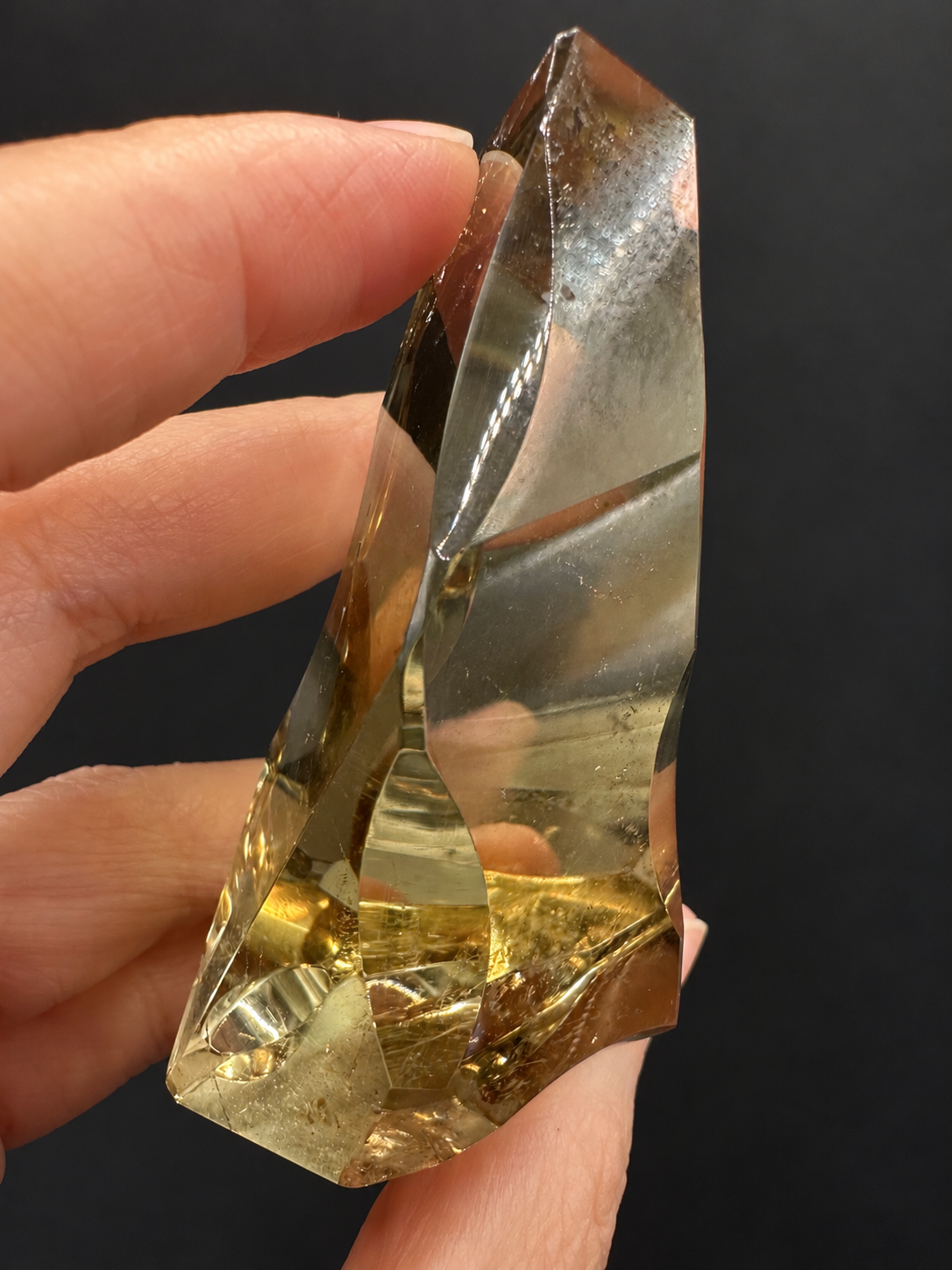 Brazilian citrine freeform No.7, 117g, approx. 7 × 5cm; slim side profile showing the crystal's depth and polished concave edges, held in the original hand against a charcoal background.