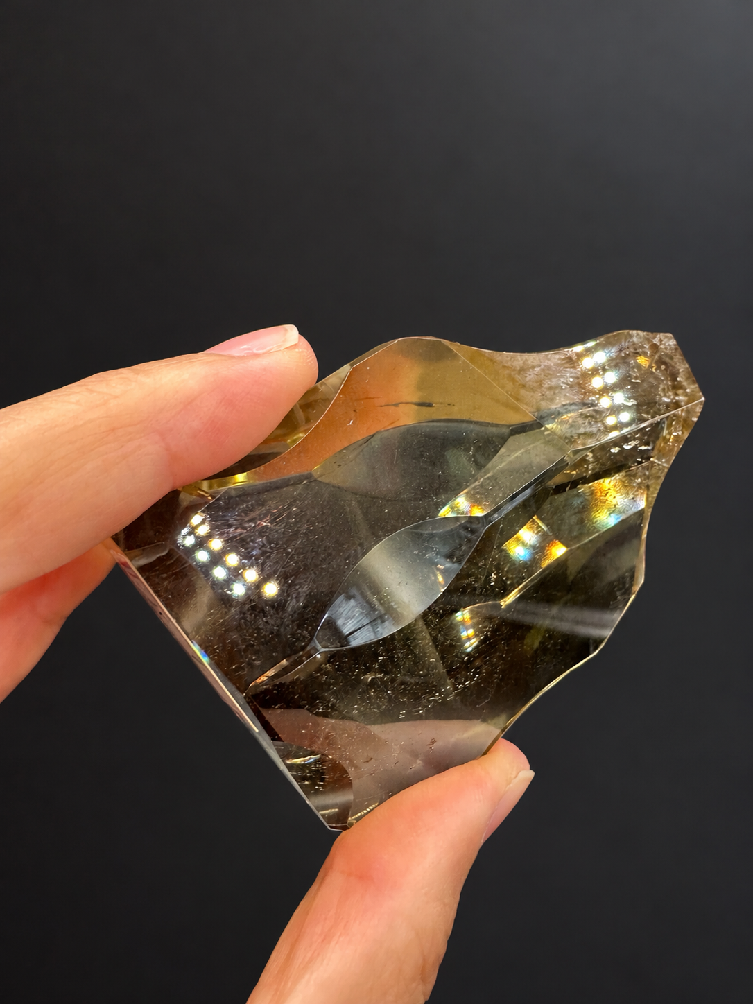 Brazilian citrine freeform No.7, 117g, approx. 7 × 5cm; upper tilted view showing the sculpted outline, fine internal details and reflections, held in the original hand against a charcoal background.