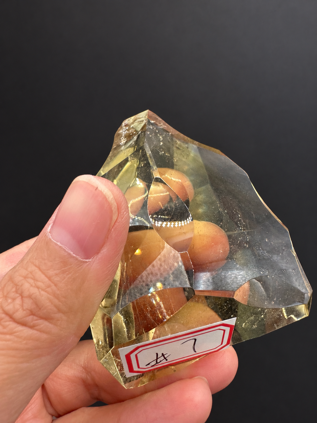 Brazilian citrine freeform No.7, 117g, approx. 7 × 5cm; labelled No.7 front view showing the asymmetric outline and original hand grip, held in the original hand against a charcoal background.