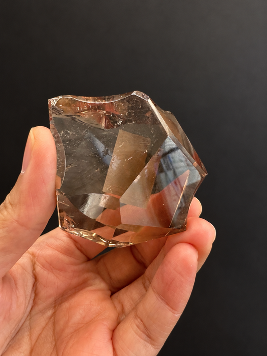 Brazilian citrine freeform No.8, 134g, approx. 5 × 5cm; broad front view showing the concave top and transparent central facets, held in the original hand against a charcoal background.