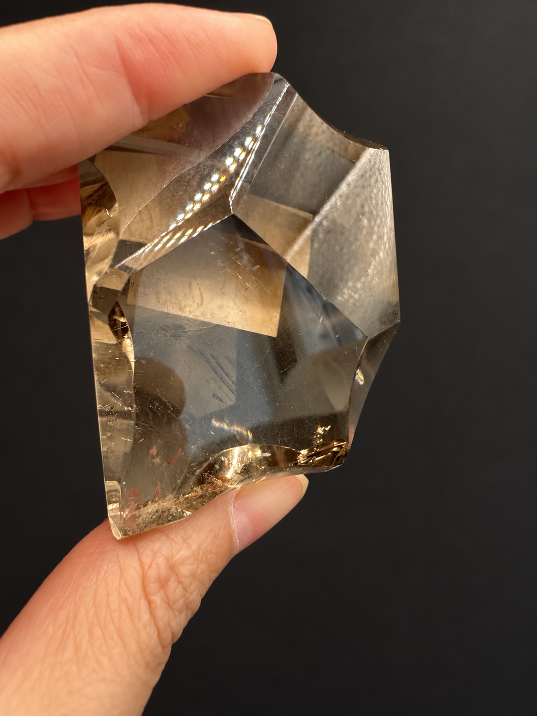 Brazilian citrine freeform No.8, 134g, approx. 5 × 5cm; close view of the concave edge, clear windows and fine internal lines, held in the original hand against a charcoal background.