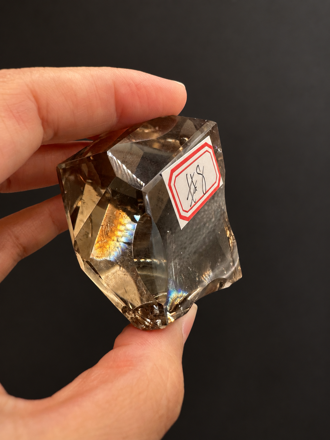 Brazilian citrine freeform No.8, 134g, approx. 5 × 5cm; angled labelled No.8 view showing polished depth and the original light reflections, held in the original hand against a charcoal background.