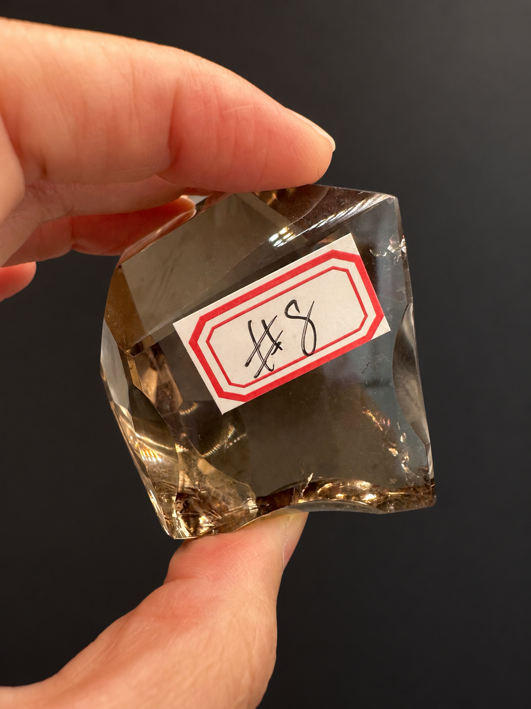 Brazilian citrine freeform No.8, 134g, approx. 5 × 5cm; close labelled No.8 view with concave lower edge and visible natural fractures, held in the original hand against a charcoal background.