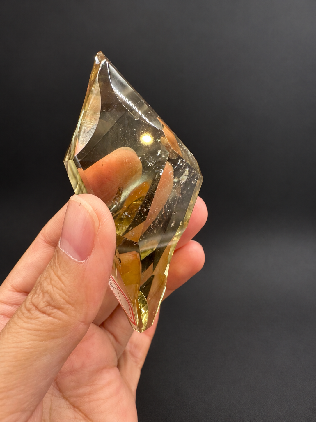 Brazilian citrine freeform No.1, 100g, approximately 8 × 4.4cm; narrow tilted view showing pointed upper edge and fine interior fractures, held in the original hand against a charcoal background.