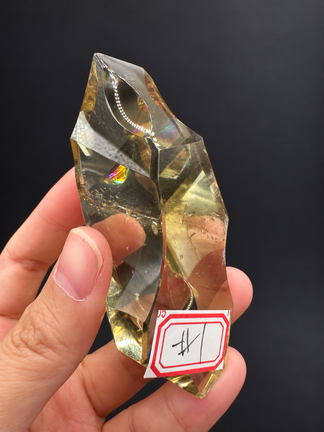 Brazilian citrine freeform No.1, 100g, approximately 8 × 4.4cm; labelled No.1 front view with original rainbow patch, pointed outline and clear central face, held in the original hand against a charcoal background.