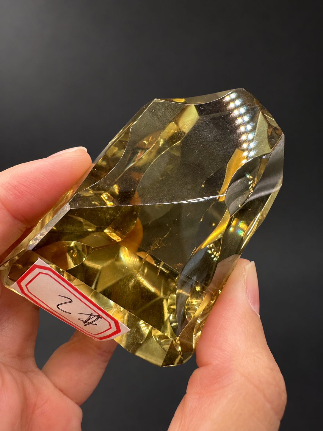 Brazilian citrine freeform No.2, 190g, approximately 8 × 4.4cm; tilted labelled identification view showing the original No.2 sticker, curved cutwork and dotted reflected lights, held in the original hand.