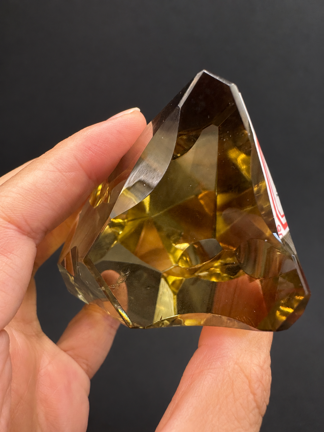 Brazilian citrine freeform No.2, 190g, approximately 8 × 4.4cm; end-on view showing the depth of the curved facets and an original label edge, held in the original hand.