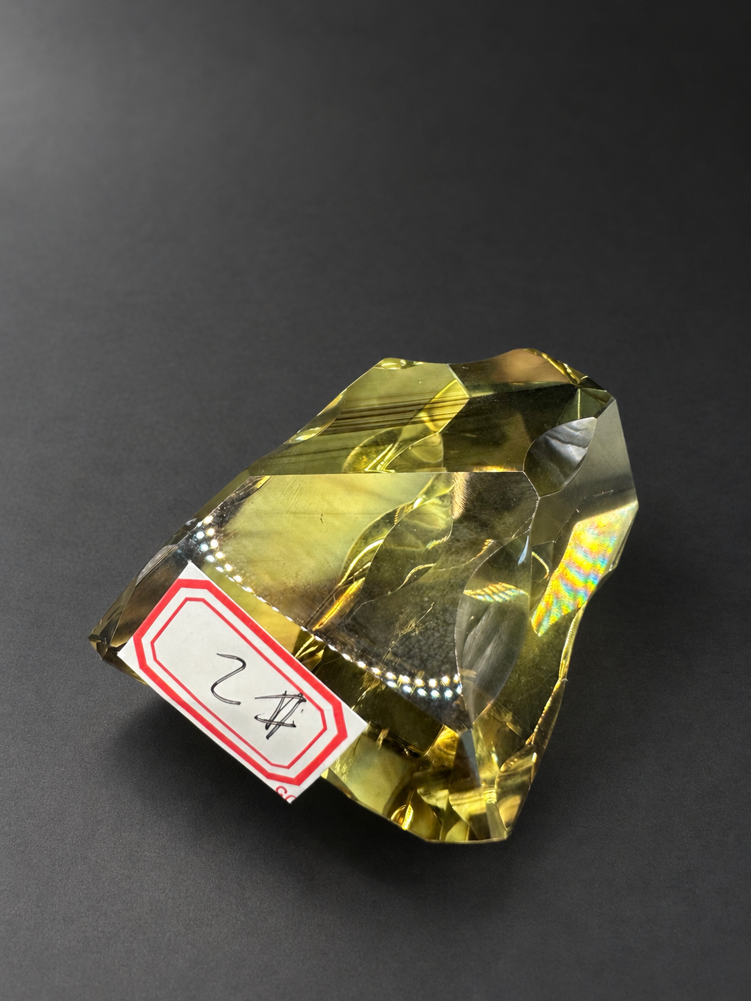 Brazilian citrine freeform No.2, 190g, approximately 8 × 4.4cm; reclining on a charcoal surface with the original red-bordered No.2 label and angle-dependent colour flashes.