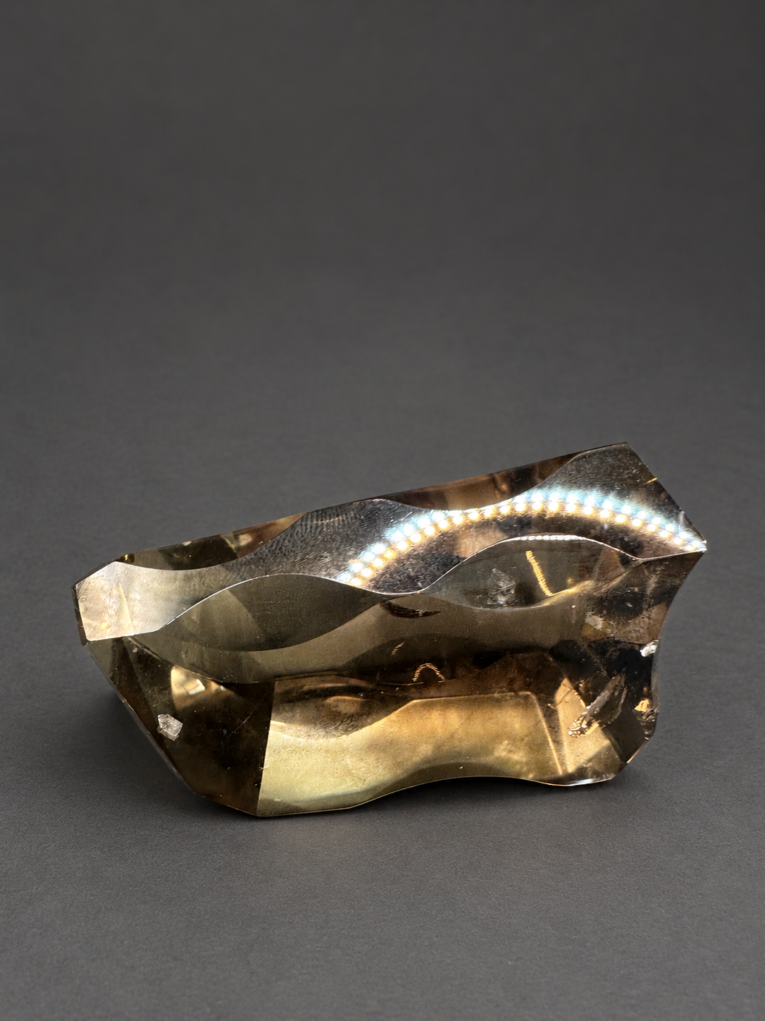 Brazilian citrine freeform No.3, 89g, approximately 7 × 4cm; horizontal view resting on its side, showing the curved profile and original reflected dotted lights, against a charcoal background.