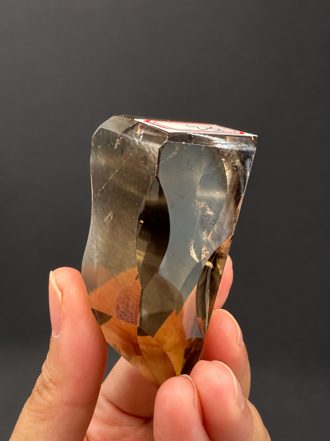 Brazilian citrine freeform No.3, 89g, approximately 7 × 4cm; upright labelled reverse angle showing intersecting facets and golden lower section, held in the original hand, against a charcoal background.
