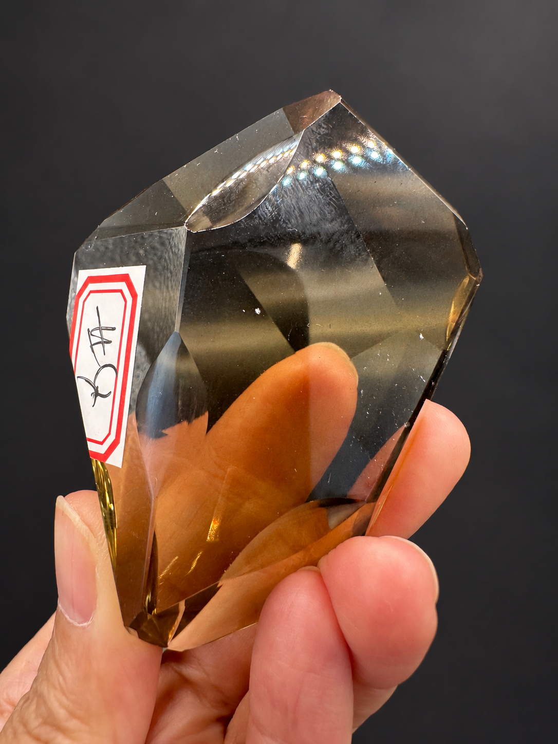 Brazilian citrine freeform No.4, 116g, approximately 8 × 5cm; upright labelled broad face showing polished concave edge and transparency, held in the original hand against a charcoal background.