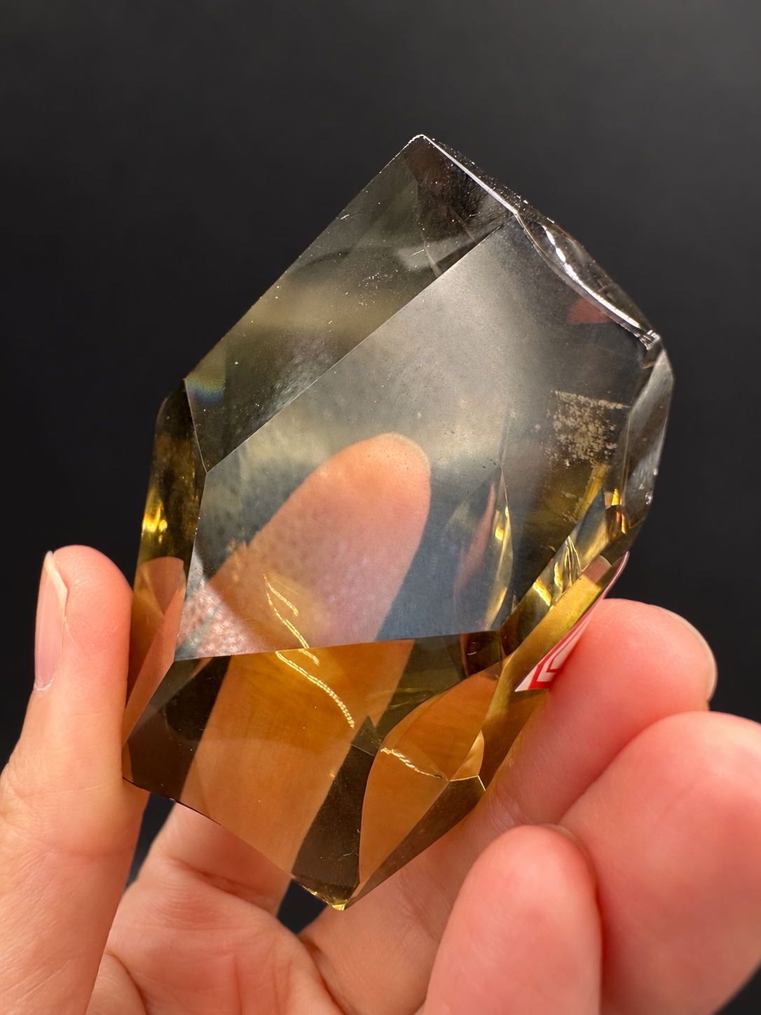 Brazilian citrine freeform No.4, 116g, approximately 8 × 5cm; reverse face showing a broad clear window with fine specks and golden lower edges, held in the original hand against a charcoal background.