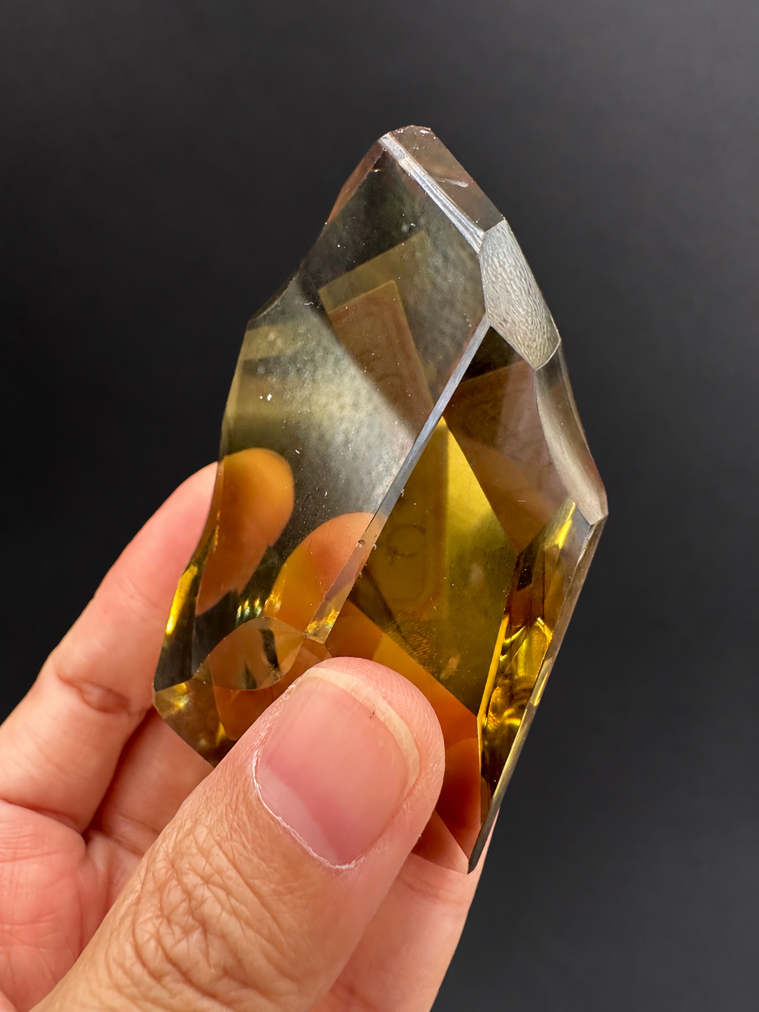 Brazilian citrine freeform No.4, 116g, approximately 8 × 5cm; side profile showing intersecting facets and deeper golden tones, held in the original hand against a charcoal background.