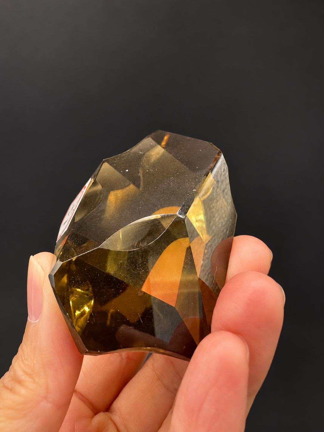 Brazilian citrine freeform No.4, 116g, approximately 8 × 5cm; lower reverse view showing curved cuts and darker golden base, held in the original hand against a charcoal background.