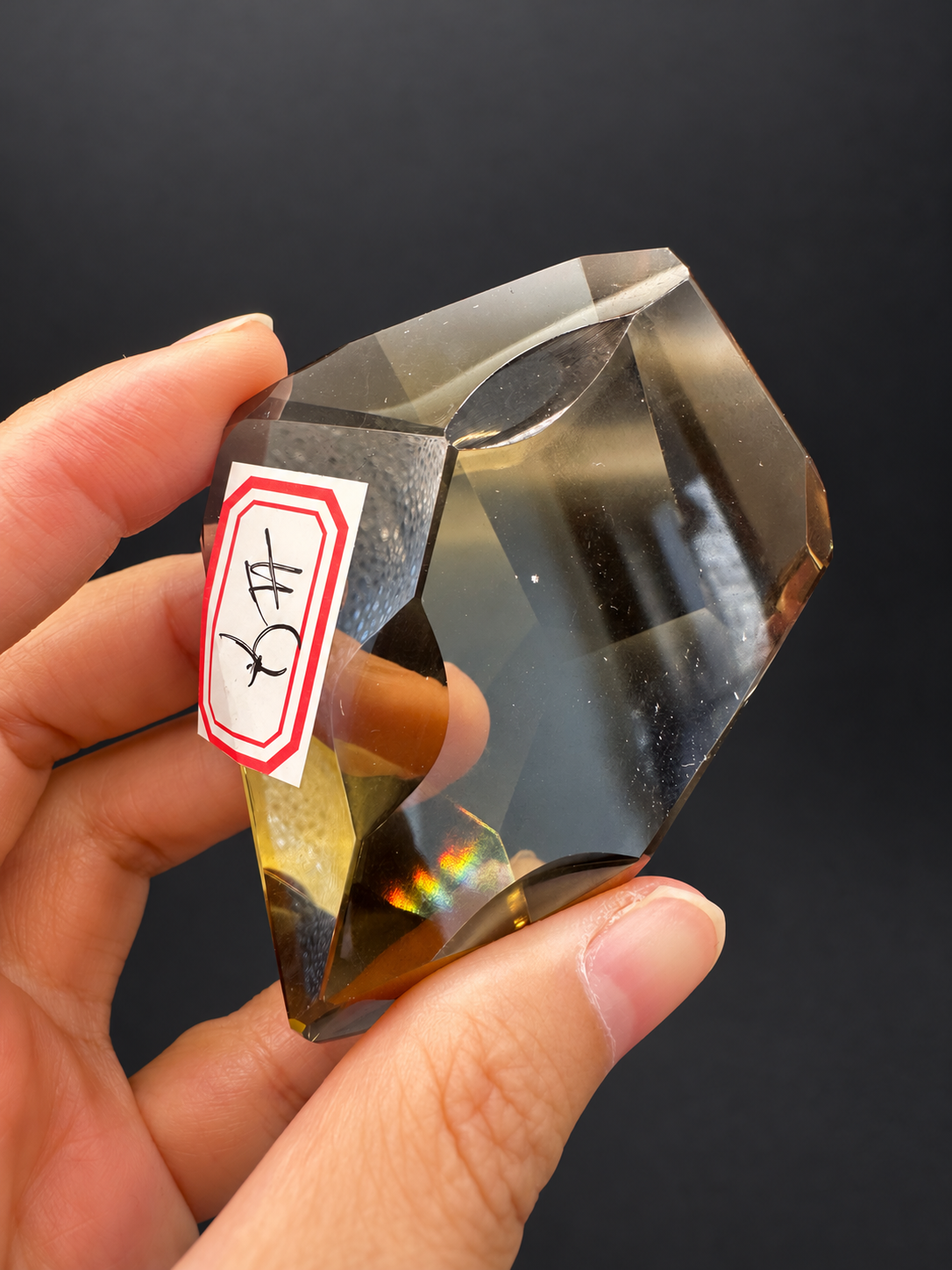 Brazilian citrine freeform No.4, 116g, approximately 8 × 5cm; labelled identification view showing clear window and original small optical flashes, held in the original hand against a charcoal background.