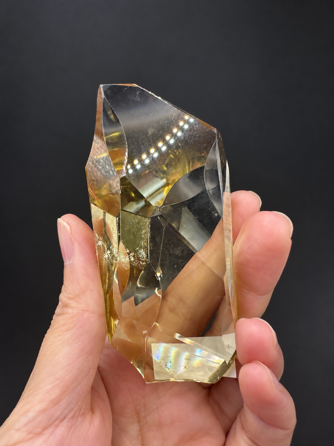 Brazilian citrine freeform No.5, 111g, approximately 9 × 4.2cm; upright opposite face showing sloping upper edge, curved cuts and visible fine fractures, held in the original hand against a charcoal background.