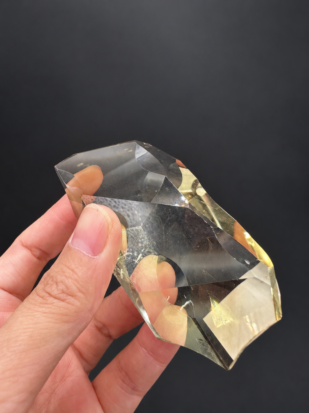 Brazilian citrine freeform No.5, 111g, approximately 9 × 4.2cm; tilted profile showing curved top, transparent body and golden base, held in the original hand against a charcoal background.