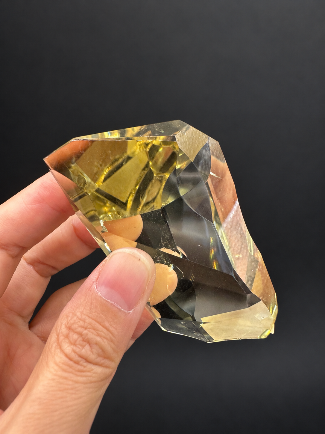Brazilian citrine freeform No.5, 111g, approximately 9 × 4.2cm; oblique close view showing a golden upper section and polished concave edges, held in the original hand against a charcoal background.