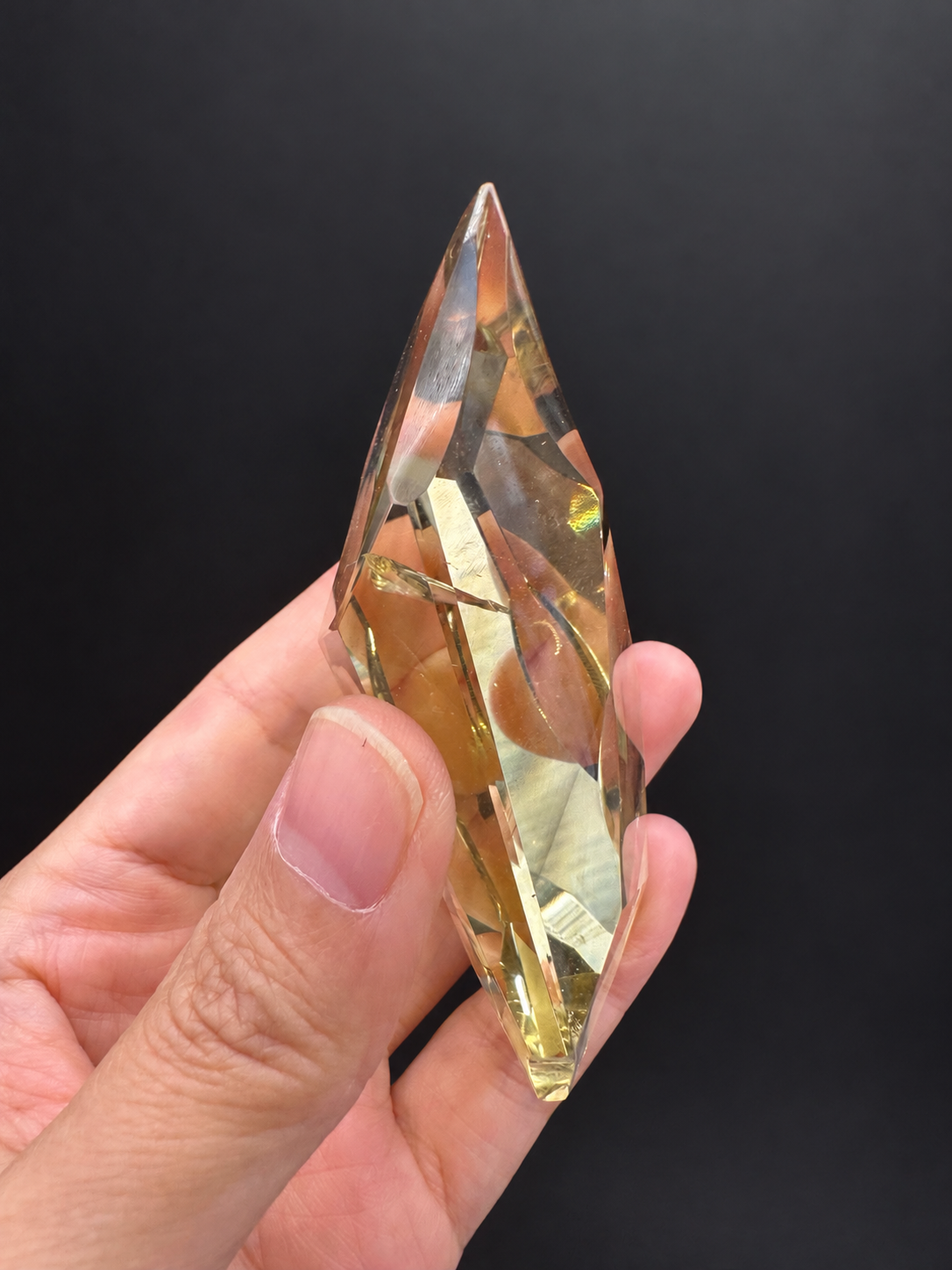 Brazilian citrine freeform No.5, 111g, approximately 9 × 4.2cm; edge-on side profile showing the thin cross-section and golden edges, held in the original hand against a charcoal background.