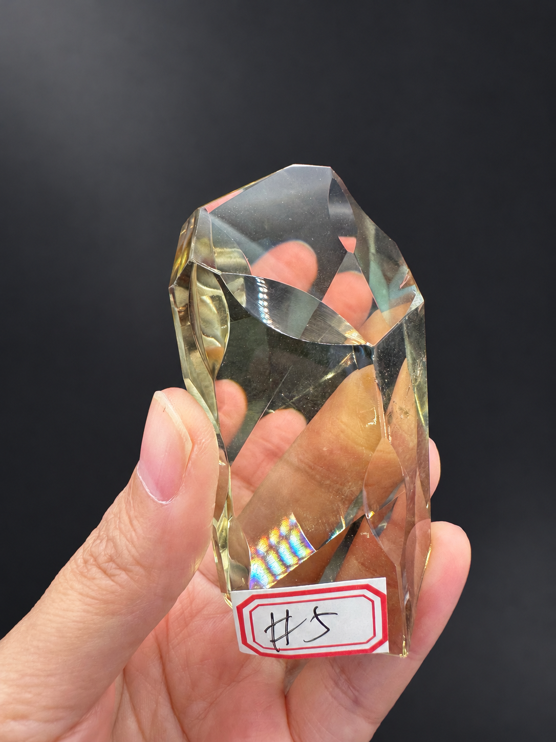 Brazilian citrine freeform No.5, 111g, approximately 9 × 4.2cm; labelled No.5 rotated front face with original optical flashes and broad clear areas, held in the original hand against a charcoal background.
