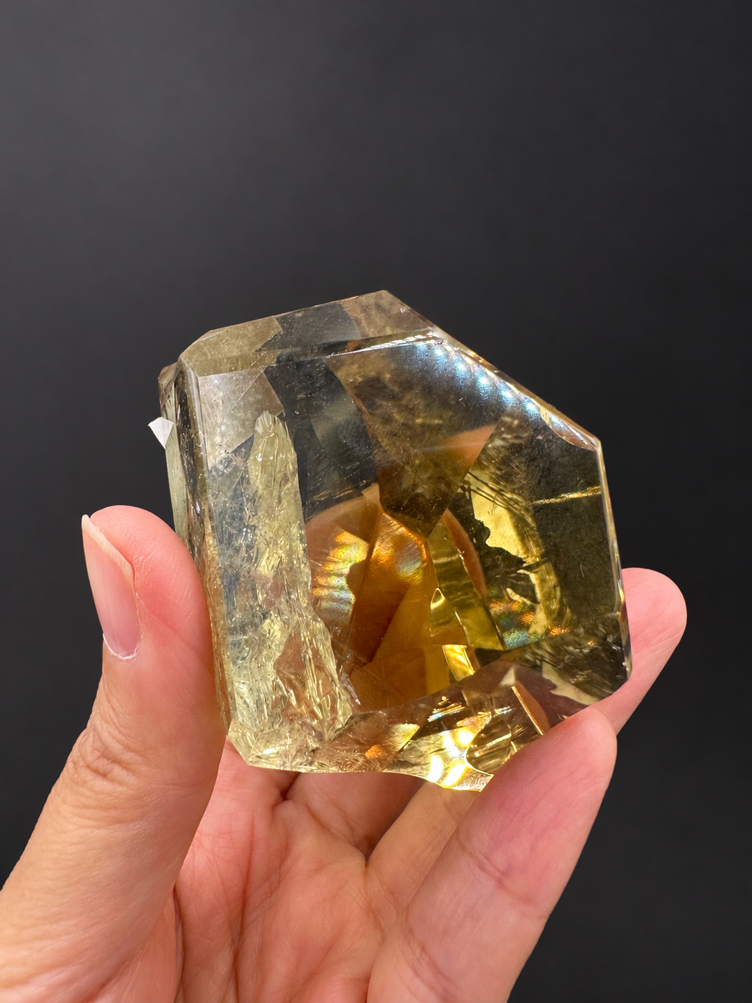 Brazilian citrine freeform No.6, 203g, approximately 6.3 × 5.8cm; reverse view with a broad champagne-clear window and golden base, held in the original hand against a charcoal background.