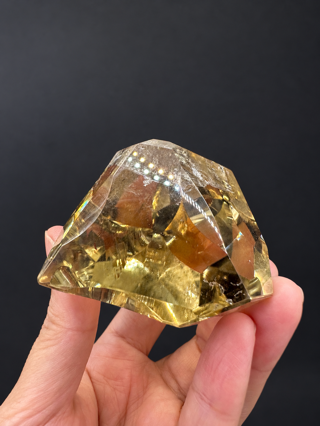 Brazilian citrine freeform No.6, 203g, approximately 6.3 × 5.8cm; horizontal bottom and depth view showing the arched cut and golden body, held in the original hand against a charcoal background.