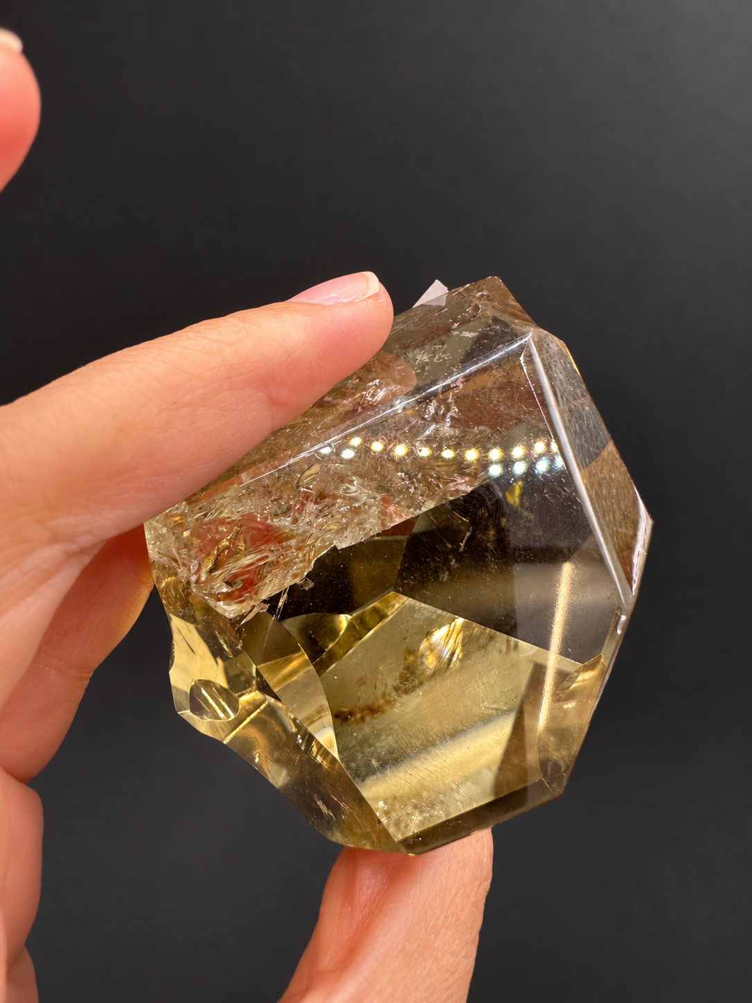 Brazilian citrine freeform No.6, 203g, approximately 6.3 × 5.8cm; tilted rear view showing feather-like fractures and a broad clear window, held in the original hand against a charcoal background.