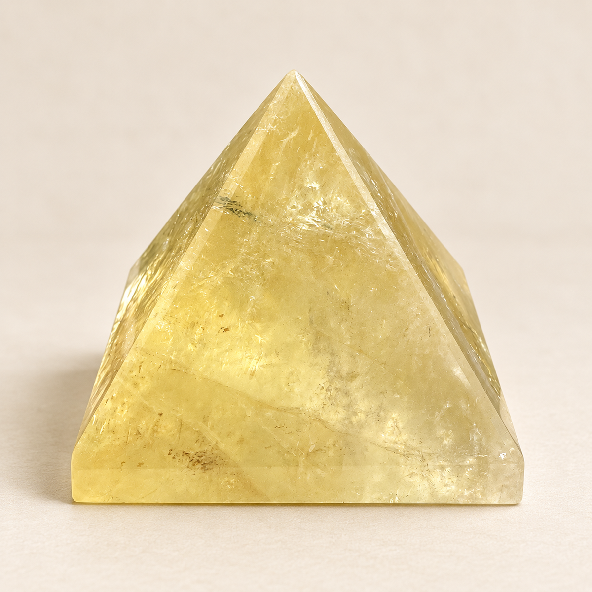 Brazilian Citrine pyramid with pale golden colour, polished triangular faces and visible internal veils on an ivory background