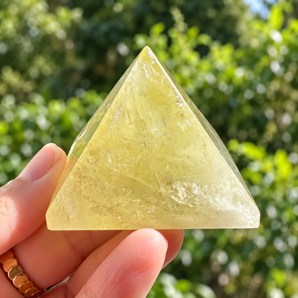 Hand-held front view of a golden Brazilian Citrine pyramid with cloudy veils in daylight
