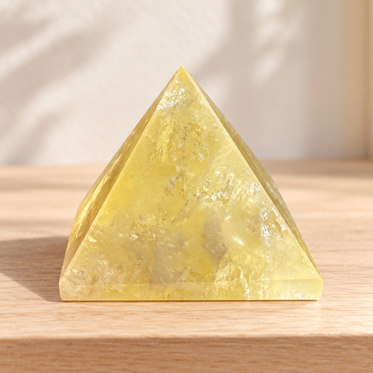 Single polished Brazilian Citrine pyramid displayed on a pale wooden shelf in soft daylight