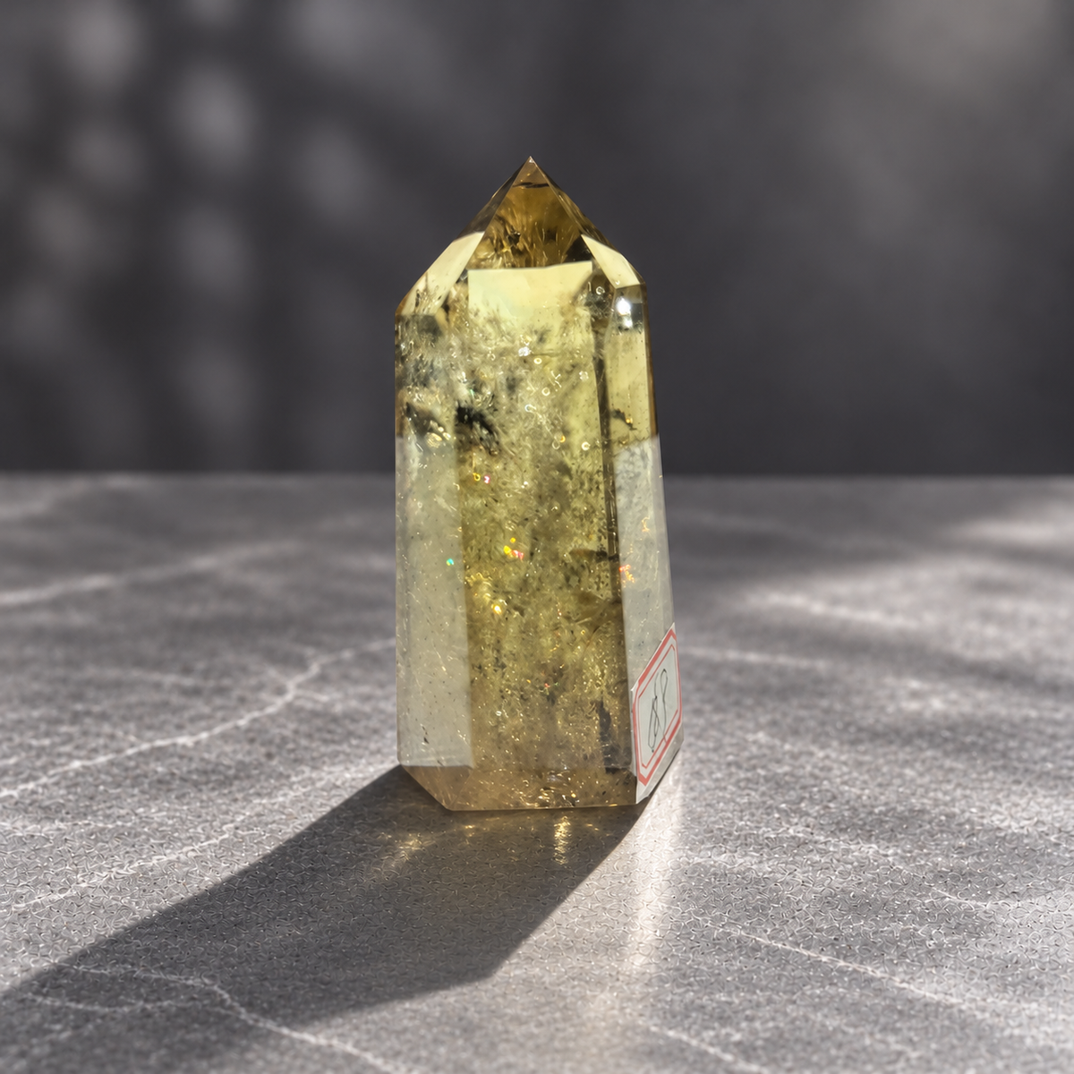 Brazilian pale yellow champagne citrine tower #8, 164g. Three-quarter view with subtle green and red rainbow glints and original label at edge