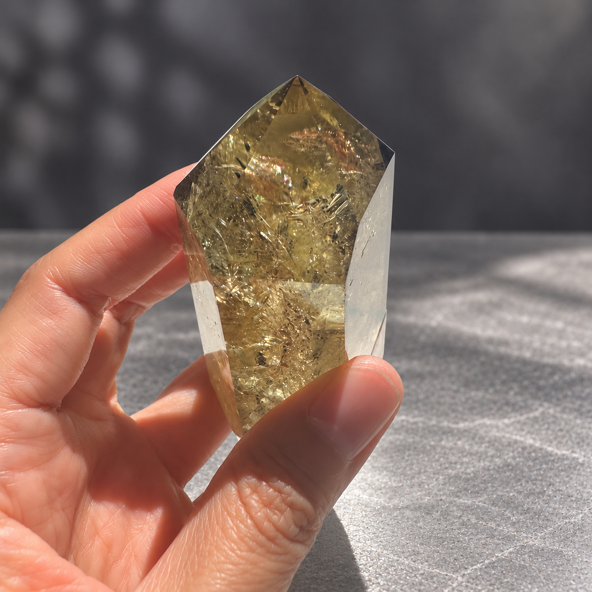 Brazilian pale yellow champagne citrine tower #8, 164g. Hand-held tilted detail showing rainbow flashes at the upper internal fracture